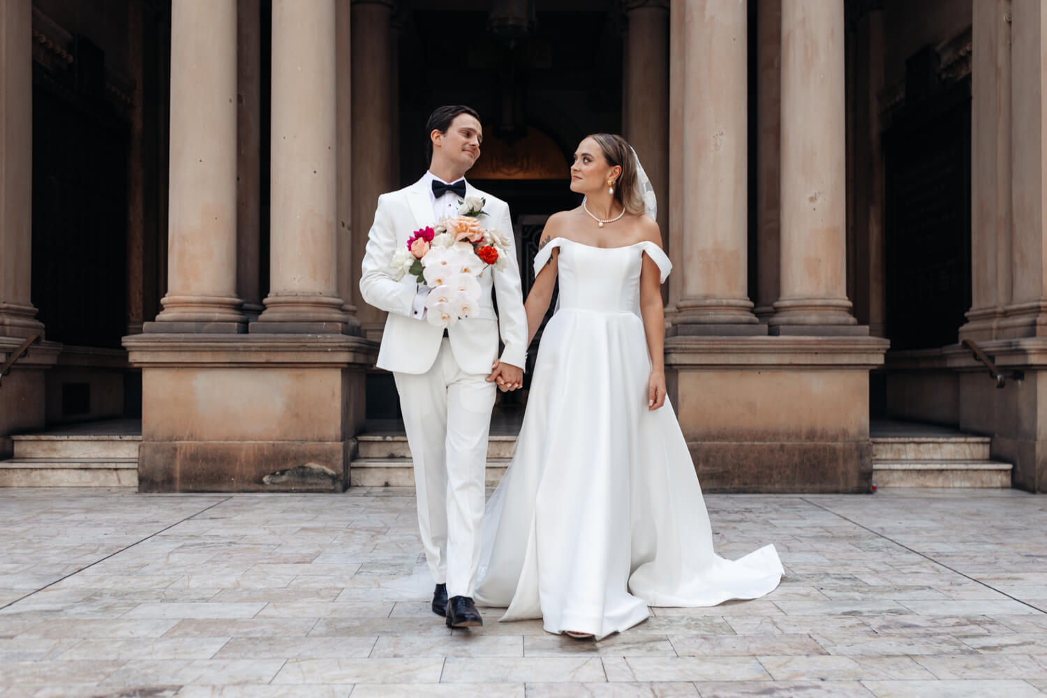 Bride and groom looking at each other as they walk away from Sydney Town Hall entrance
