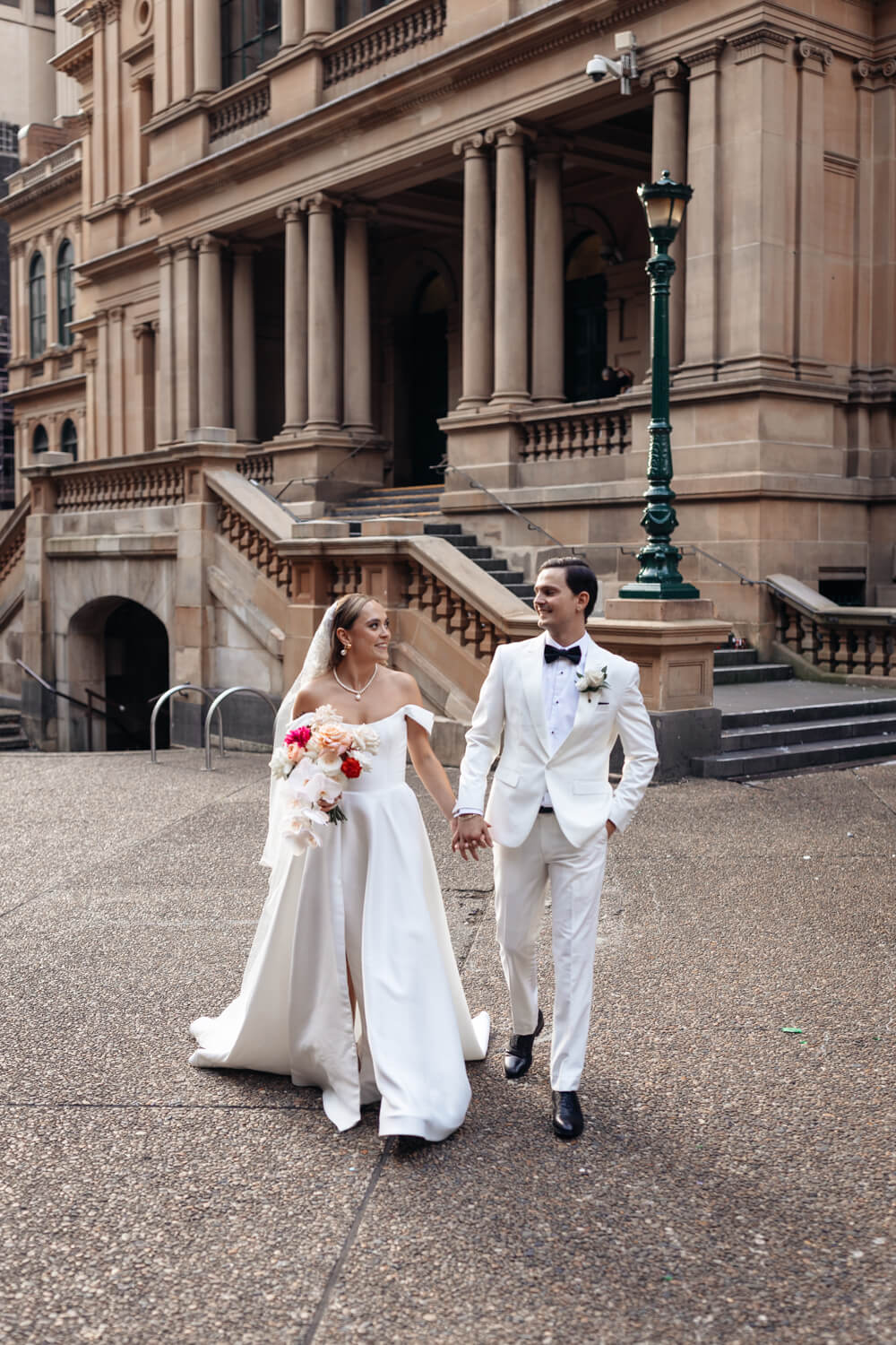 Bride and groom walking hand in hand outside Sydney's Town Hall