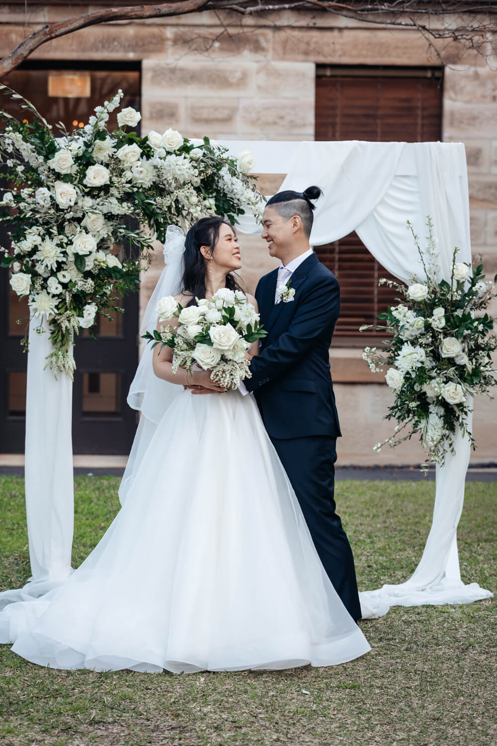Bride and groom standing beneath their arbour during their wedding at The Mint