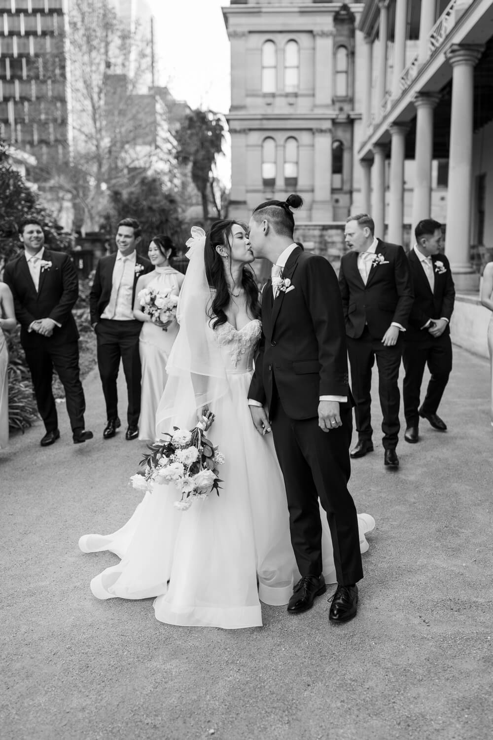Bride and groom kissing in front of their bridal party at The Mint in Sydney during their wedding