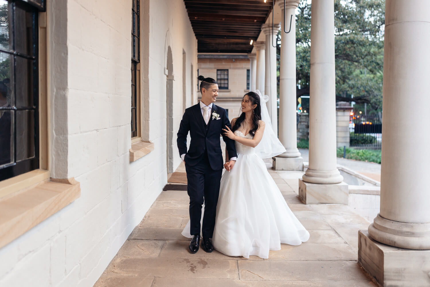 Bride and groom walking along the fron balcony of the Sydney Mint During their wedding day