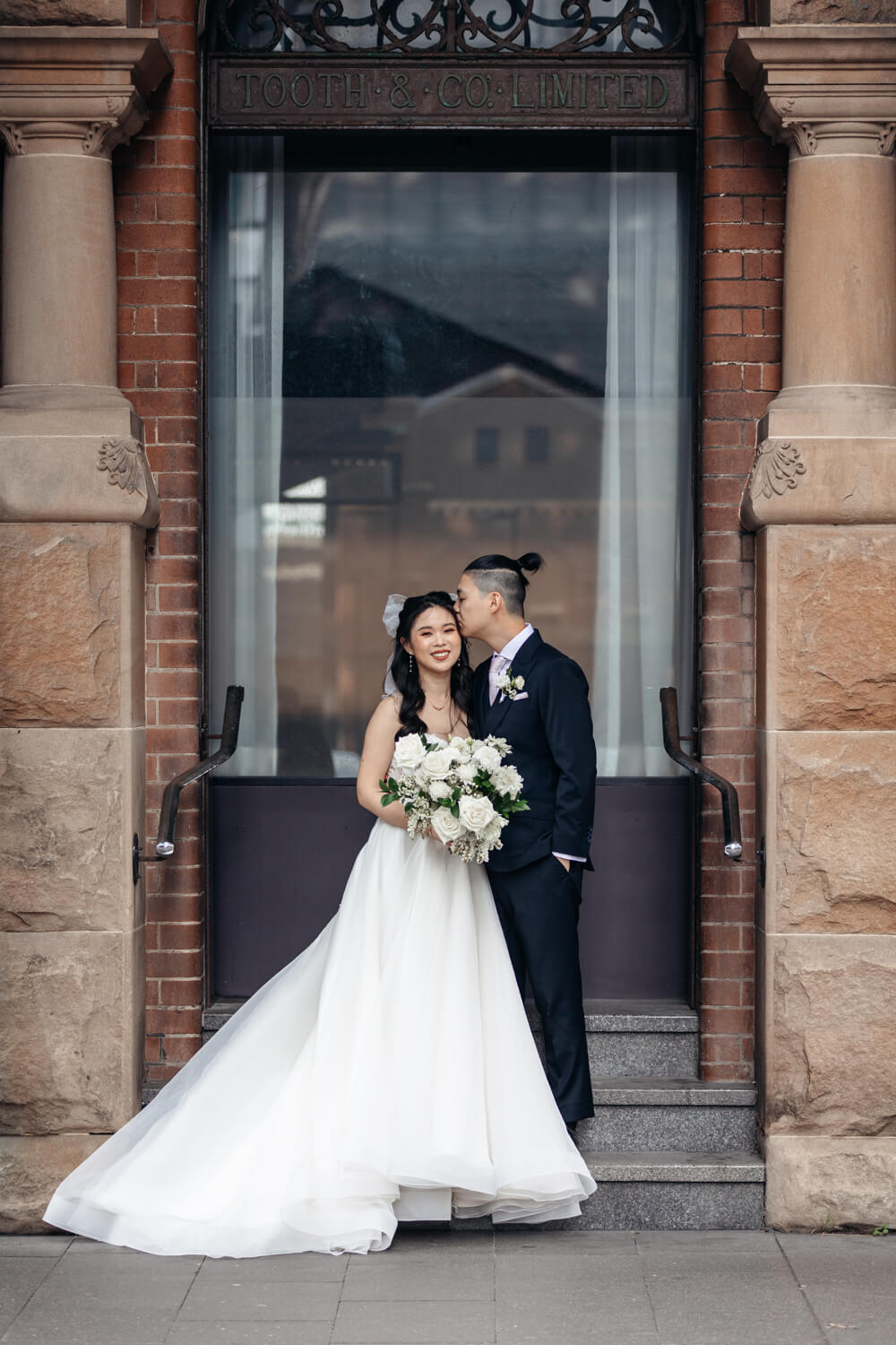 Groom kissing his bride on the cheek on their wedding day outside The Old Clare Hotel in Sydney