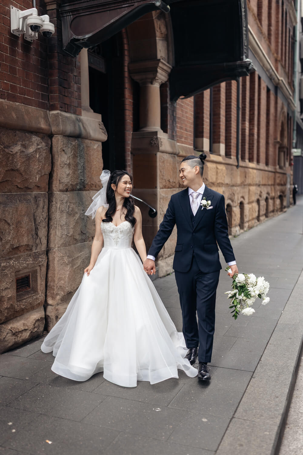 Bride and groom holding hands and walking in the street outside The Old Clare Hotel in Sydney on their wedding day